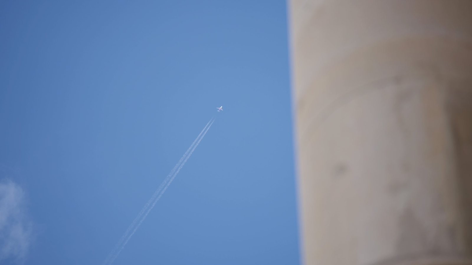A plane crossing a clear sky beside a pale stone column