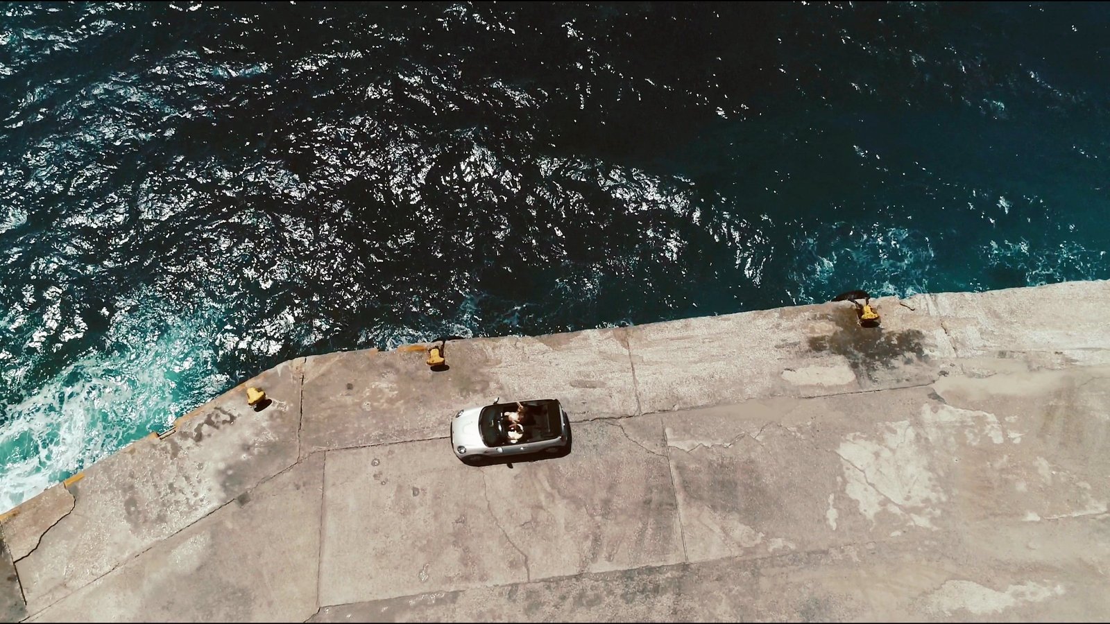 A white open-top car on a sea platform above the water, seen from above