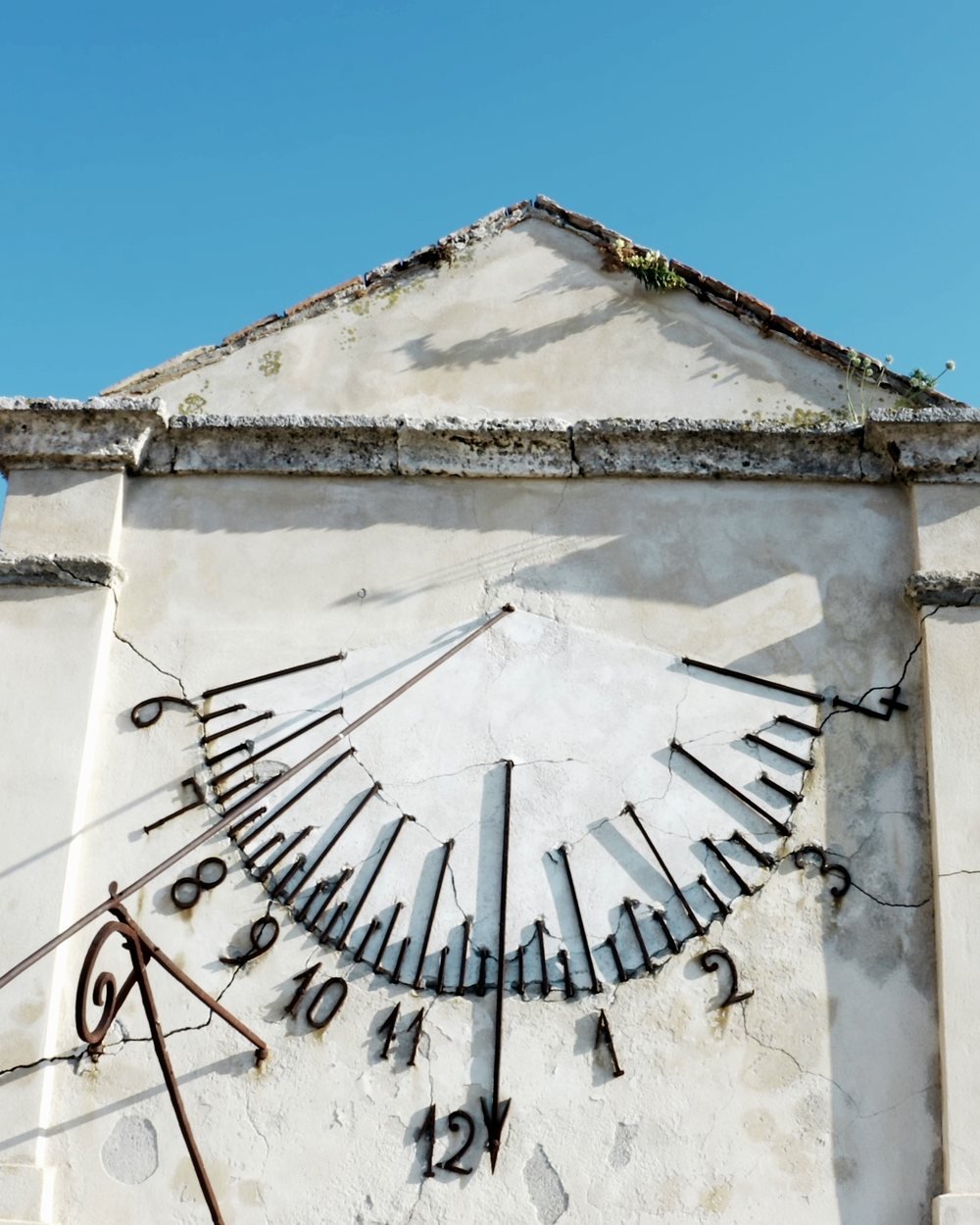 A sundial on a plaster wall, the hours in iron, in hard morning sun