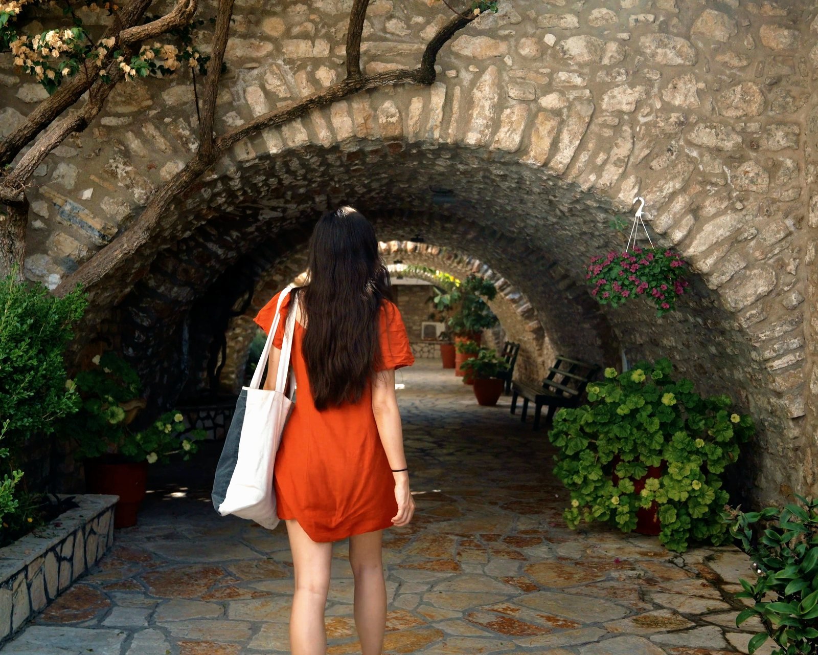 A woman walks under a stone arch into a courtyard of flowers