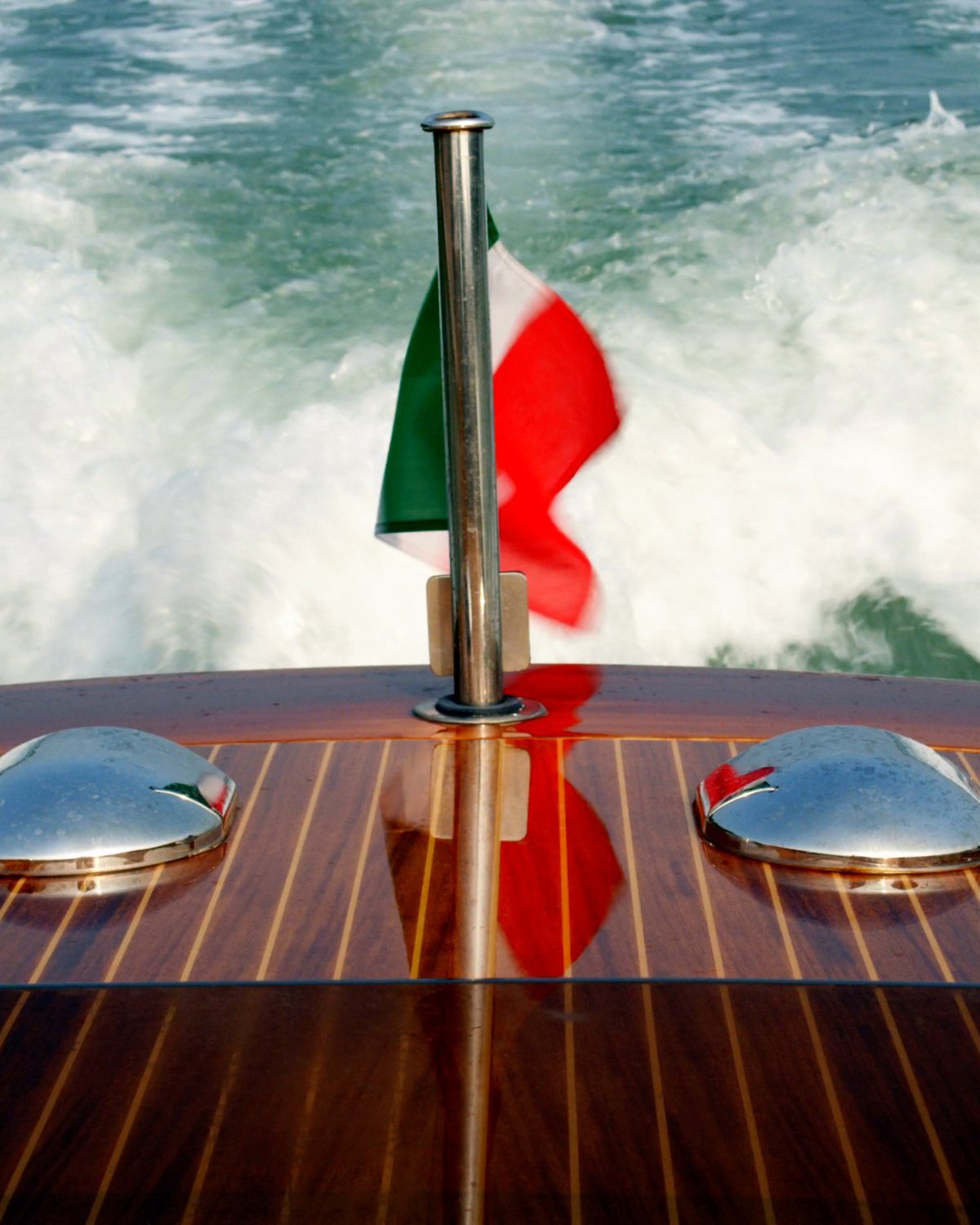 The mahogany stern of a classic launch, its flag and white wake behind