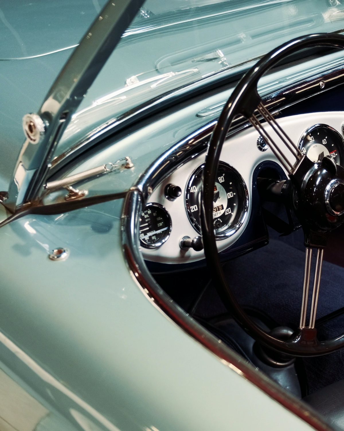 The cockpit of a pale blue roadster: a wooden wheel and cream dials